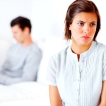 Upset woman sitting away from male reading on sofa looking away